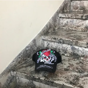 Svart keps med döskalle - Cool svart keps med broderad döskalle, hjärta och texten 'Love Slow' framtill. Färgglada detaljer i rött, grönt och vitt. Nät på baksidan för extra ventilation och böjd skärm. Perfekt accessoar för en edgy streetstil.