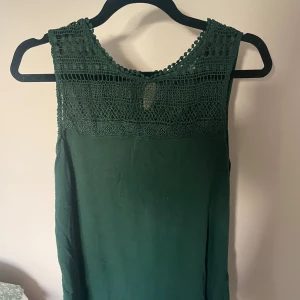 Emerald green ärmlös blus 🫒 - Supersnygg mörkgrön blus med ärmlös design och detaljerad spets upptill. Blusen har rund halsringning och en liten knapp i nacken. Perfekt för dig som gillar en enkel men ändå elegant look. Älskar att ha i skolan eller på tjejmiddag 🪐🍋‍🟩