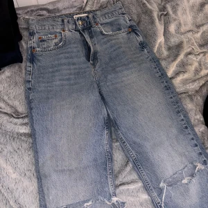 Ljusblå ripped jeans från Gina - Säljer ett par ljusblå jeans från Gina med raka ben och snygga slitningar på båda knäna. Jeansen har hög midja, klassiska fem fickor och dragkedja med knapp. Perfekt för dig som gillar en avslappnad och trendig look.