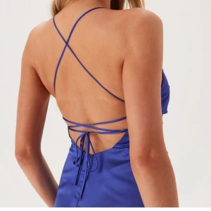 Blå balklänning med snörning - Snygg blå balklänning i satinliknande material med smala axelband som korsas i ryggen och snörning. Klänningen har en slits framtill och draperad överdel som ger en elegant siluett. Använd två gånger på nians avslutnings middag. Väldigt bra skick!  Orginal pris 899kr