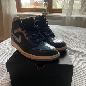 Nike Air Jordan 1 Mid SE Craft Obsidian - Nike Air Jordan 1 Mid SE Craft i färgen Obsidian/White-French Blue. Snygga high-top sneakers med mix av skinn och textil, grå swoosh och blå detaljer. Klassisk snörning och vit sula. Perfekta för dig som gillar streetstyle och vill sticka ut.