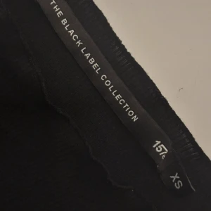 Svart långärmad topp  - En svart långärmad topp från The Black Label Collection (lager157)  i storlek XS. Modellen är figurnära med rund halsringning och lätt ribbad struktur. Perfekt att styla med jeans eller kjol för en clean look.