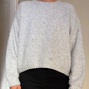 Ljusgrå stickad tröja  - Mjuk och stickad tröja i ljusgrått. Tröjan har en enkel, ribbad struktur och rund halsringning. Den har två fläckar som syns på sista bilden.