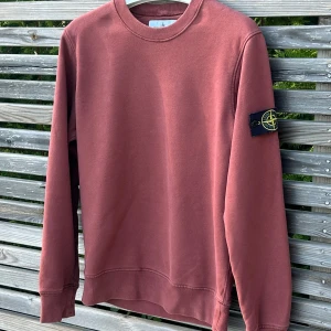 Terrakotta sweatshirt från Stone Island - Säljer en snygg terrakotta sweatshirt från Stone Island med klassisk patch på ärmen. Tröjan har rund hals, långa ärmar och ribbade muddar. Tillverkad i mjuk bomull för skön passform och sicket är 8/10