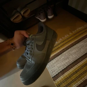 Nike Air Force 1 mörkgrå sneakers - Säljer ett par mörkgrå Nike Air Force 1 sneakers med klassisk siluett och svart swoosh. Skorna har snörning och coola neongula detaljer med flera små swoosh-loggor på hälen. Ovandelen är i syntet och textil, perfekt för dig som gillar streetstyle.
