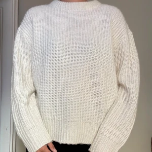 Vit stickad tröja med rund hals - En vit stickad tröja med rund hals och breda muddar. Tröjan har en loose passform och långa ärmar.