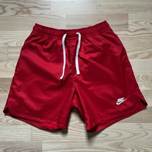 Röda Nike shorts med snörning - Snygga röda shorts från Nike med vit snörning i midjan och klassisk logga på benet. Perfekta för sommaren och träning, tillverkade i lätt syntetmaterial som torkar snabbt. Sportig look och bekväm passform. Köpta på Zalando 
