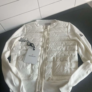 Moncler cardigan - Snygg vit dunväst från Moncler med quiltad framsida och ribbstickade ärmar. Perfekt för dig som gillar stilrena och lyxiga plagg. Skriv för mer info