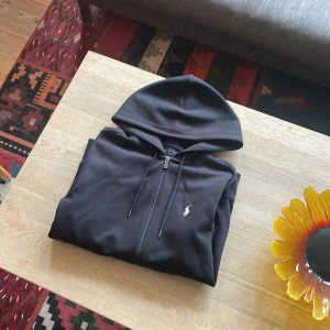 Svart hoodie från Polo Ralph Lauren - Svart kofta från Polo Ralph Lauren, värde 1600kr. Inga defekter, använts varsamt och riktigt skön. Har inte använt den på länge säljer den därför. Tveka inte på att skriva vid fundering. 