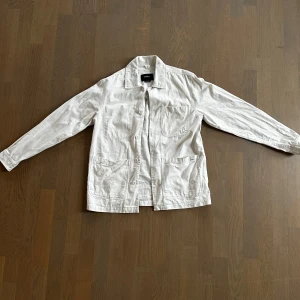 Vit overshirt från Pull&Bear - Säljer en stilren vit overshirt från Pull&Bear i bomull. Jackan har tre stora fickor framtill, knäppning med knappar och klassisk krage. Perfekt för lager-på-lager och enkel att matcha med olika outfits.