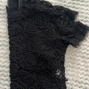 Svart spetskofta från Zara Trafaluc - Supersnygg svart kofta från Zara Trafaluc med vacker spets och broderade detaljer. Koftan har korta ärmar, dragkedja i ryggen och en unik struktur som ger en cool look. Perfekt för dig som vill sticka ut lite extra!