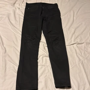 Svarta jeans från Tiger of Sweden - Snygga svarta jeans från Tiger of Sweden med klassisk femficksdesign och diskreta logodetaljer vid fickan. Jeansen har rak passform och är tillverkade i ett mjukt bomullsmaterial med lite stretch för extra komfort. Mycket bra skick inga skador! Skriv mer för andra bilder eller information. Modellen är slim fit