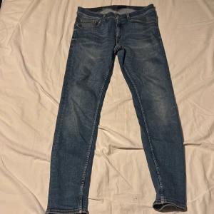 Blå jeans från Tiger of Sweden - Snygga blå jeans från Tiger of Sweden med klassisk femficksdesign och raka ben. Jeansen har en mellanblå tvätt med lätt slitning och är tillverkade i bomull. Perfekta för dig som gillar stilrena och tidlösa jeans. OBS! har haft ett hål vid skrevet men igen sytt syns inte när man har på sig dem. Skriv för fler bilder på tillexempel när ja har på mig dem