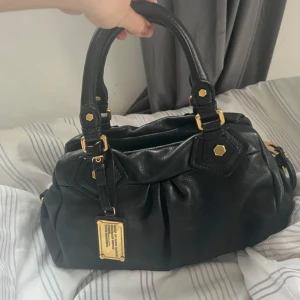 Marc Jacobs väska -  Snygg svart handväska i skinn från Marc by Marc Jacobs med gulddetaljer. Kommer med ett extra handtag om man vill ha den längre, men kan även användas som en kortare handväska. Väskan är i väldigt bra skick och säljer pågrund utav att den inte kommer till användning längre. Pris kan diskuteras vid snabba affärer! 💕