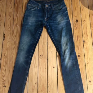 Mörkblå Nudie Jeans - Snygga mörkblå jeans från Nudie Jeans med klassiska orange sömmar och läderpatch bak. Modellen är ”Skinny lin” Jeansen har en tight passform och är i en snygg tvätt. En liten defekt vid en av fickorna. Storlek: W28 L30, vill man ha fler bilder så är det bara att skriva! Perfekta för dig som gillar en stilren och modern look⭐️