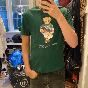 Grön Polo Bear t-shirt från Ralph Lauren - Snygg grön t-shirt från Ralph Lauren med ikoniska Polo Bear-trycket på bröstet. Storlek 14-16 barn storlek men passar som xs hör av er om frågor kring fler bilder eller storleksfrågor
