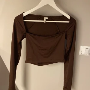 Brun croppad topp från NLY Trend S - Säljer en brun långärmad croppad topp från NLY Trend, storlek S. Modellen har en fyrkantig ringning och är figurnära med stretchigt material i polyester och elastan.
