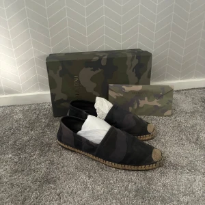 Valentino Garavani espadrilles camouflage - Snygga espadrilles från Valentino Garavani i mörkgrönt och svart camouflage-mönster. Perfekta för dig som vill sticka ut med en lyxig och trendig touch.