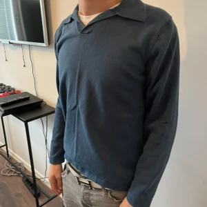 Mörkblå långärmad pikétröja - Säljer en stilren mörkblå pikétröja med klassisk krage och lång ärm. Tröjan är i mjukt bomullsmaterial och har en enkel, clean look utan synliga loggor eller detaljer. Perfekt för dig som gillar minimalistisk stil.