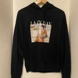 Svart hoodie med tryck - Svart hoodie med coolt tryck framtill där det står 'LAZY DAY' och en konstnärlig bild av en kvinna. Tröjan har huva med snörning och långa ärmar. Perfekt för chill dagar och en avslappnad stil.☺️