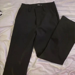 Svarta kostymbyxor från BikBok - Stilrena svarta kostymbyxor från BikBok i klassisk rak modell. Byxorna har hällor för bälte, snedställda fickor och stängs med dragkedja och knapp. Perfekta för en clean och dressad look.