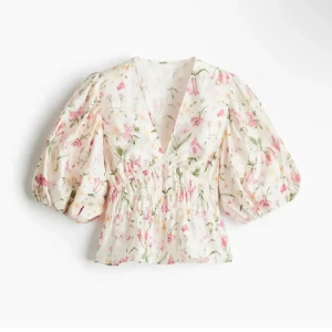Blommig blus med puffärm - Supersöt blommig blus med v-ringning och stora puffärmar. Blusen är vit med rosa och gröna blommor, har smock i midjan och en luftig, lätt känsla. Perfekt för dig som gillar romantisk och trendig stil.