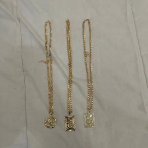 Tre guldiga halsband med drakmotiv - Säljer tre snygga halsband i guldfärg med kedjor och unika drakberlocker. Två av hängen är rektangulära, varav ett har glittriga stenar runt kanten, och det tredje är runt med detaljerad drake. Perfekt accessoar för dig som vill sticka ut.