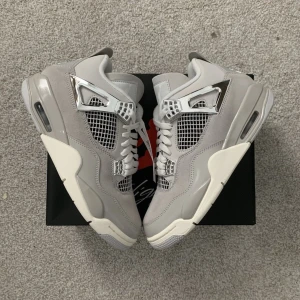 Nike Air Jordan 4 Retro Metallic Silver - Nike Air Jordan 4 Retro i grå mocka och skinn med silvriga metalldetaljer och vit sula. Skorna har meshpaneler, snörning och ikonisk Jumpman-logga under sulan. Snygg och stilren sneaker med coola detaljer som sticker ut.
