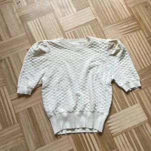Vit quiltad tröja från Knit Mix - Säljer en vit quiltad tröja från Knit Mix i storlek M. Tröjan har puffiga axlar, ribbade muddar och ett snyggt rutmönster i materialet. Perfekt för dig som gillar en stilren men ändå unik look.
