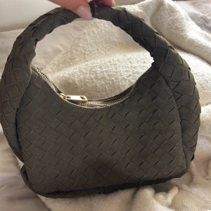Olivgrön flätad liten väska. - Snygg olivgrön väska med flätad design och rundad form. Lyxig känsla och perfekt för dig som vill ha en stilren detalj till din outfit.
