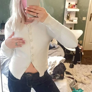 Vit kofta med pärlknappar - Superfin vit kofta med långa ärmar och söta pärlknappar framtill. Koftan är stickad och har en klassisk, lite croppad passform. Perfekt att slänga över en topp för en söt och stilren look.