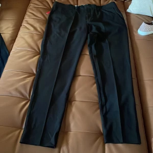 Svarta kostymbyxor från Repreve - Stilrena svarta kostymbyxor från lindbergh med klassisk rak passform. Byxorna har pressveck framtill och är tillverkade i ett mjukt, lätt material som ger en dressad look. Perfekta för dig som gillar en clean och tidlös stil.