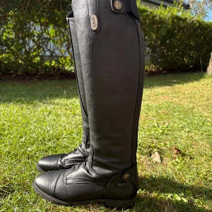 Svarta ridstövlar i skinn från CRW - Säljer ett par svarta ridstövlar från CRW i äkta skinn. Stövlarna har klassisk design med snörning framtill och dekorativa sömmar. Perfekta för dig som vill ha stilrena och funktionella stövlar till ridning.
