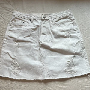 Vit jeanskjol från H&M - Snygg vit jeanskjol från H&M i storlek 36. Kjolen har slitna detaljer, fransad nederkant och klassiska fickor både fram och bak. Gjord i 100% bomull med en normal passform och knappstängning framtill 🤍