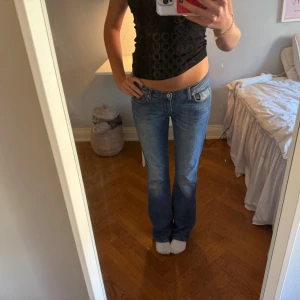 Blå bootcut jeans från Weill, storlek 29 - Snygga blå jeans från Weill i bootcut-modell med låg midja. Klassisk femficksdesign och ljus tvätt med subtila slitningar. Jeansen har gul detalj på bakfickan och är tillverkade i mjukt denim-material som sitter skönt och ger en avslappnad look.