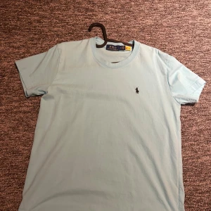 Polo Ralph Lauren T-shirt ljusblå - Snygg ljusblå t-shirt från Polo Ralph Lauren med klassisk broderad logga på bröstet. T-shirten är i mjuk bomull och har en normal passform med korta ärmar och rund hals. Perfekt basic-plagg med stilren vibe.