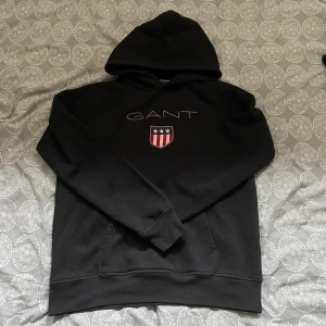 Svart hoodie från GANT - Svart hoodie från GANT i storlek 176 - sitter som en S. Passar mig som är ca 180. Hoodien är använd 1-2 gånger och därmed är den i ett extremt bra skick. Nypris: 1600kr. Mitt pris: 149kr
