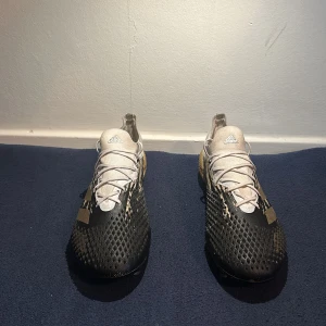 Adidas predator 20.1  low fg  - Säljer ett par Adidas fotbollsskor med cool design i svart, vitt och guld. Skorna har snörning, mönstrad ovandel och dobbar för bra grepp på planen. Ovandelen är i syntetmaterial och skon har en sportig look med tydlig Adidas-logga på plösen.