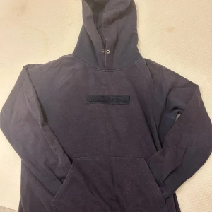 Mörk blåa hoodie från Peak Performance - Svart hoodie från Peak Performance med broderad logga på bröstet. Klassisk modell med huva, dragsko och känguruficka framtill. Tillverkad i mjuk bomullsmix, perfekt för chill eller streetwear.