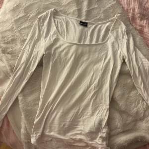 Vit långärmad topp Gina Tricot XS - En basic vit långärmad topp från Gina Tricot i storlek XS. Toppen har en rundad, djup urringning och är gjord i mjuk bomull. Perfekt att styla med jeans eller kjol för en clean look.