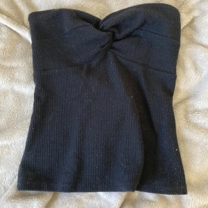 Svart ribbad tubtopp Stockh LM Studio - Svart ribbad tubtopp från Stockh LM Studio i storlek XS. Toppen har twistad detalj framtill och en liten silverring bak. Gjord i stretchigt material som sitter snyggt och bekvämt. Perfekt att styla med jeans eller kjol för en trendig look.