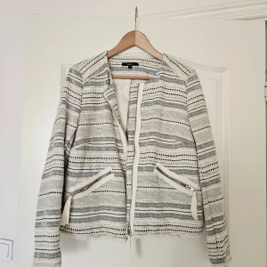 Randig overshirt från Lindex - Snygg randig overshirt från Lindex i vitt och svart med dragkedja framtill och två fickor med dragkedjor. Jackan har en rak passform, lång ärm och är tillverkad i ett vävt material med fransad nederkant för en cool touch.