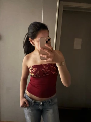 Vinröd bandeau tubtopp med paljetter - Snygg vinröd bandeau tubtopp med glittriga paljetter och broderade detaljer upptill. Toppen är axelbandslös och har en tight passform, Materialet känns mjukt och stretchigt. Har aldrig kommit till användning men finns ingen prislapp kvar.