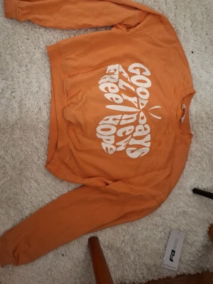 Orange croppad sweatshirt med tryck - Säljer en orange croppad sweatshirt med vitt tryck i form av en fjäril och texten 'GOOD DAYS FLY FREE NEW HOPE'. Tröjan har rund halsringning och långa ärmar. Perfekt för dig som gillar färg och statement-plagg. Bra skick och inte mycket använd men lite knottrig