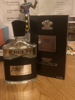 Creed Aventus Eau de Parfum 100ml - Creed Aventus Eau de Parfum i 100 ml flaska. Flaskan är genomskinlig med svart band och silverdetaljer, inklusive en elegant etikett med ryttare och texten Aventus. Kommer med svart och silver kartong som matchar flaskans exklusiva design.