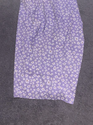 Lila blommig kjol  med slits - Supersöt lila omlottkjol med vita små blommor och en snygg slits framtill. Kjolen har en dragsko i sidan som ger en cool rynkad effekt. Perfekt för dig som vill ha en feminin och trendig look.