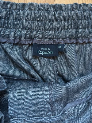 Grå kostymbyxor från KappAhl - Snygga grå kostymbyxor från KappAhl med elastisk midja och diskret fiskbensmönster. Byxorna har rak passform och är perfekta för en clean och stilren look. Tillverkade i mjukt material som känns bekvämt hela dagen.