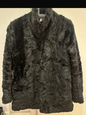 Svart fejk pälsjacka tiger of Sweden stl S - Mysig svart pälsjacka med hög krage och lång ärm. Jackan har en rak passform och är tillverkad i mjuk fuskpäls som ger en lyxig känsla. Perfekt för att hålla värmen under kyliga dagar och ger en trendig look till din outfit.