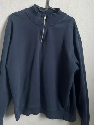 Mörkblå half-zip hoodie från RYLS - Mörkblå hoodie från RYLS med halv dragkedja framtill och hög krage. Tillverkad i mjukt sweatshirtmaterial och har en avslappnad passform. Perfekt för en chill och stilren look.