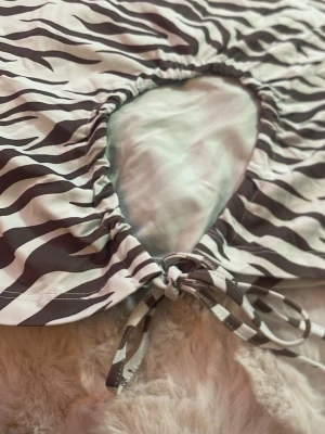 Zebramönstrad croppad topp med knyt - Trendig croppad topp med zebramönster i brun och vitt. Toppen har korta ärmar, en rund cut-out framtill och knytband vid midjan bak i rygg ett runt hål för extra detalj. Perfekt för dig som vill sticka ut med en cool och djurinspirerad look.